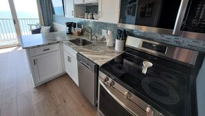 Una cocina moderna con armarios blancos, una estufa de acero inoxidable y un amplio ventanal con vistas a un balcón.