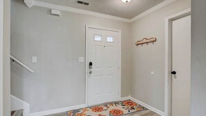A hallway with a white door, a small rug with floral patterns, and a coat rack with hooks.
