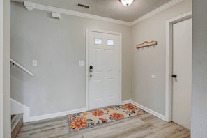 A hallway with a white door, a small rug with floral patterns, and a coat rack with hooks. - Modern House by Indy Motor Speedway w/3BR  (Indianapolis)