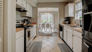 A kitchen with white cabinets, a stove, a sink, and a dining area with chairs and a table.