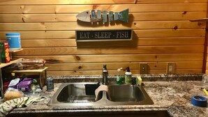 Una cocina con pared de madera, un lavamanos y un cartel que dice 'EAT - SLEEP - FISH'.