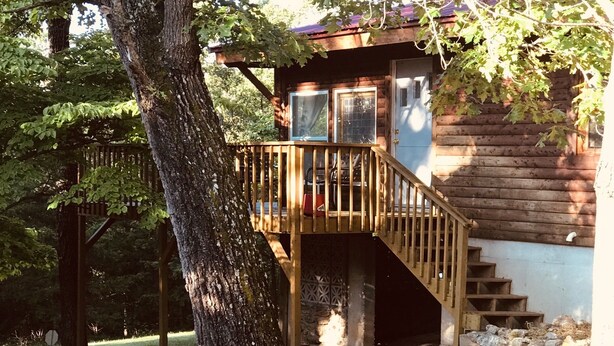 Una cabaña de madera con una escalera de madera que conduce a una terraza, rodeada de árboles.