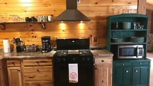 Una cocina con paredes de madera, una estufa negra, un microondas y una cafetera.