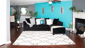 Un salon avec un canapé noir, un tapis à motifs et un mur d’accent de couleur turquoise.