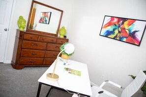 A room with a white desk, a chair, a wooden dresser, and a colorful painting on the wall. - 8 min from the airport, located right off exit (college park)