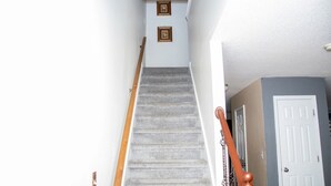 Un escalier avec une rampe en bois, des marches recouvertes de moquette et deux tableaux encadrés accrochés au mur.