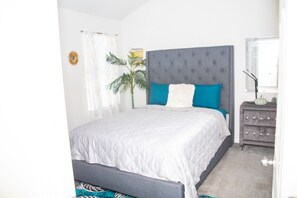 A bedroom with a bed, a nightstand, a plant, and a window. - 8 min from the airport, located right off exit (college park)