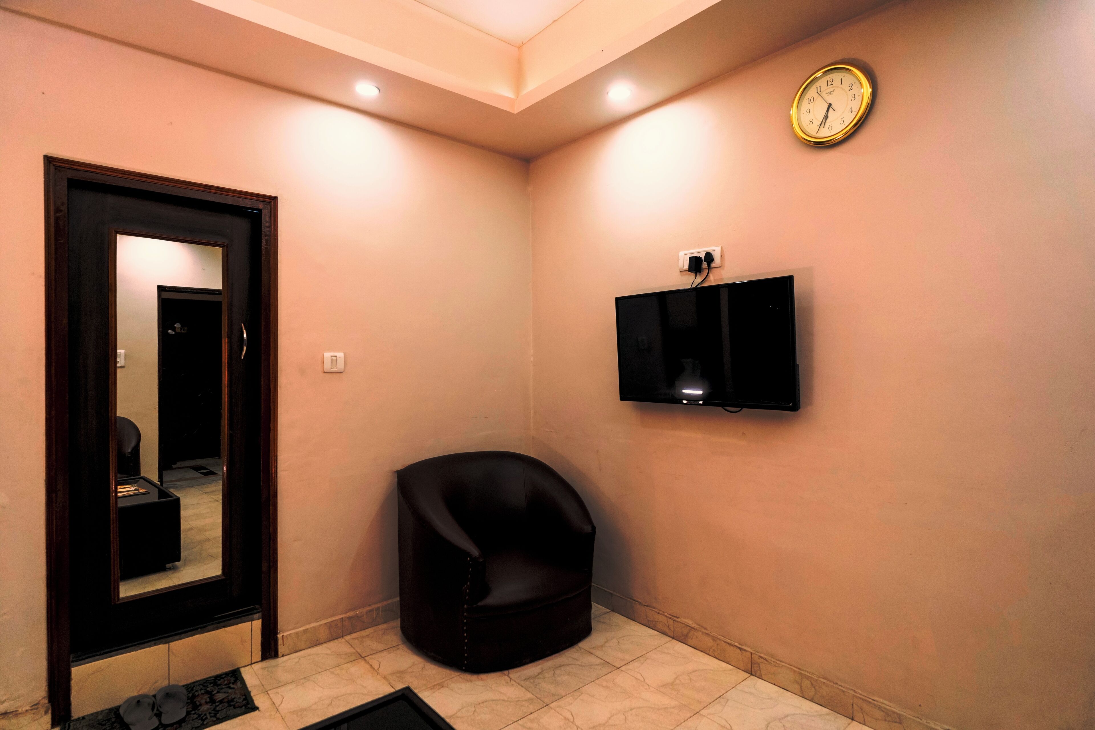 A room with a black leather chair, a clock on the wall, and a television mounted above a cabinet.