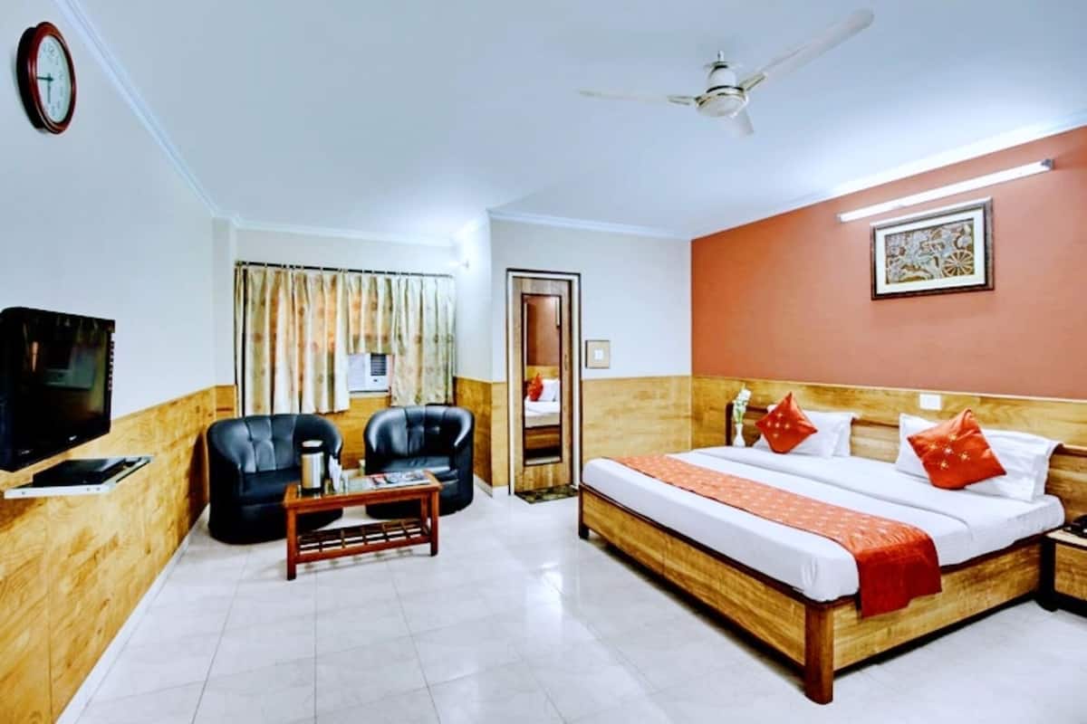 A hotel room with a bed, a TV, a coffee table, a chair, a ceiling fan, and a window with curtains.