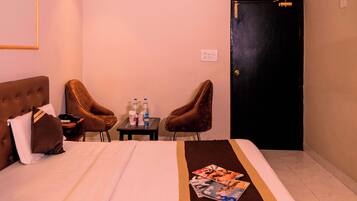A hotel room with a bed, two armchairs, a small table with bottles, and a door.