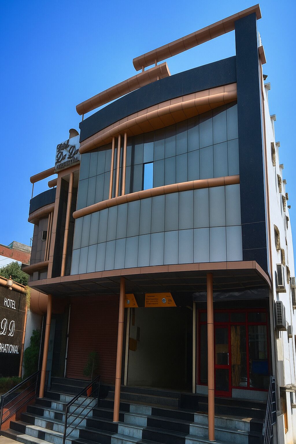 A modern hotel with a prominent entrance, a staircase leading to the lobby, and a clear sky in the background.