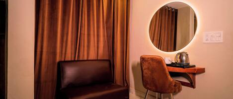 Una habitación con un sofá de cuero marrón, un escritorio de madera con una silla, un espejo redondo con luz y un reloj en la pared.