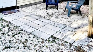 Ein überdachter Patio-Bereich mit zwei Adirondack-Stühlen, einem kleinen Schuppen und einem Holzzaun.