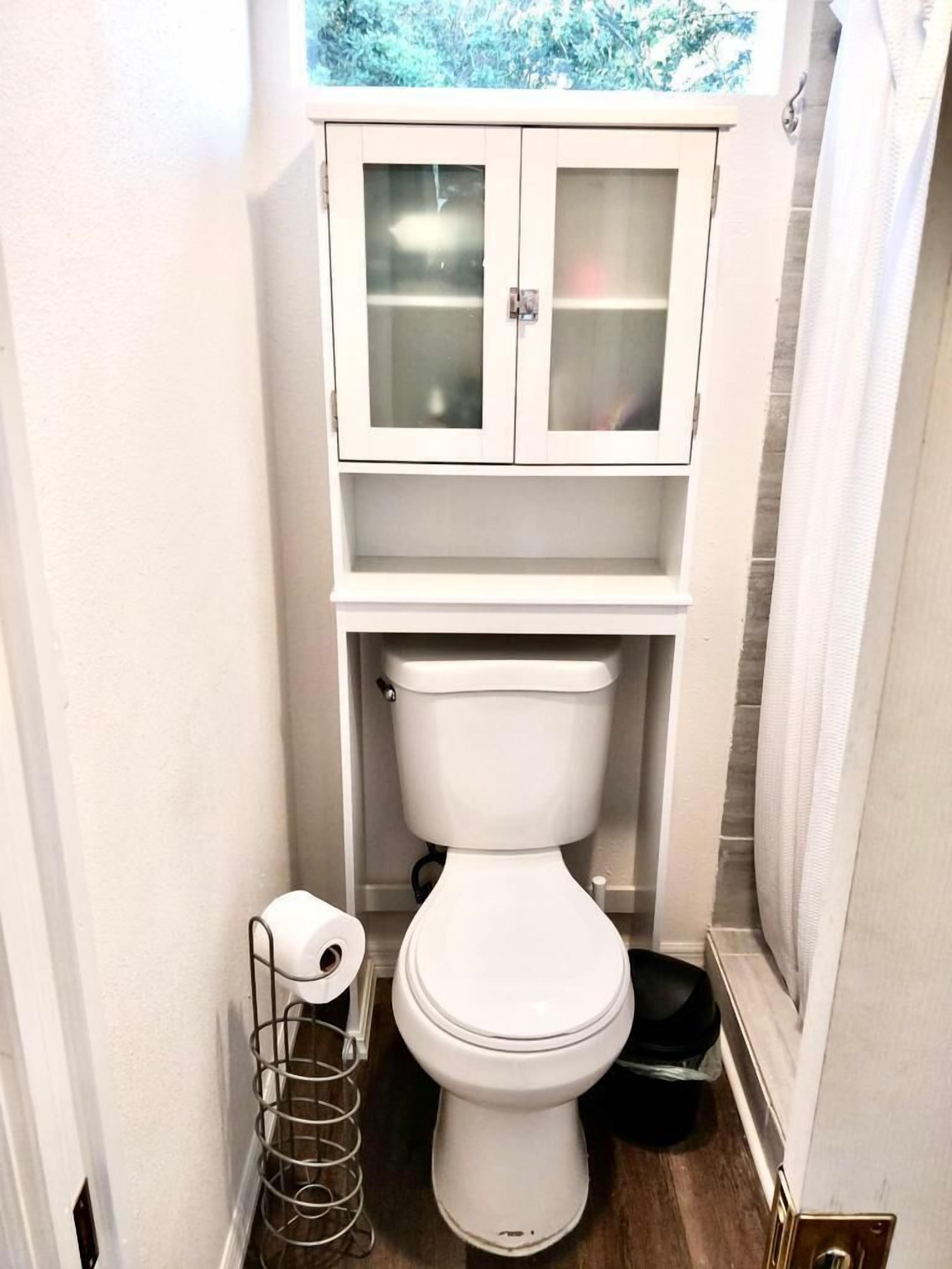 Une petite salle de bain comprenant des toilettes, un meuble avec des portes en verre et un porte-rouleau de papier toilette en métal.
