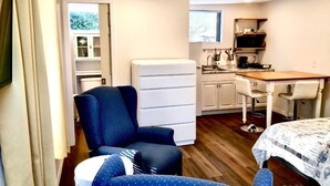 Ein kleines Zimmer mit Bett, Schreibtisch, Stuhl, einer kleinen Küchenzeile und einem Fenster.