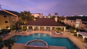 A hotel with a swimming pool, lounge chairs, and a covered patio area.