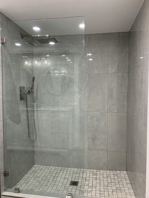 A modern shower area with a glass enclosure, a handheld showerhead, and a control panel.