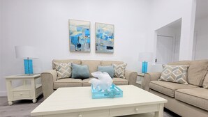 A living room with two sofas, a coffee table, and two side tables with lamps. There are two framed artworks on the wall.
