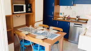 Een kleine keuken met een magnetron, koffiezetapparaat en een spoelbak. Er staat een eettafel gedekt met borden en glazen.