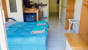 Een kleine kamer met een bed, een tafeltje en een kitchenette.
