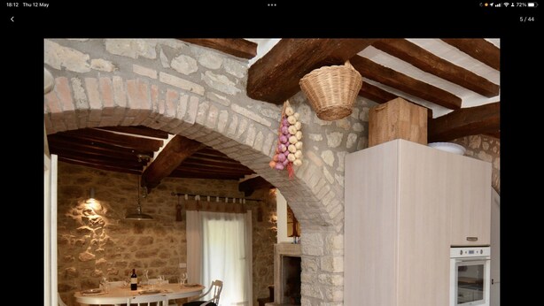 Una cocina rústica con paredes de piedra, vigas de madera, un cesto colgante y un comedor con mesa y sillas.