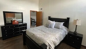 Quarto com cama, cômoda, mesa de cabeceira, ventilador de teto e espelho.