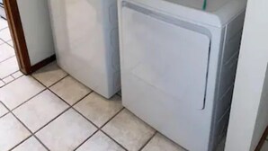 Uma lavanderia com duas máquinas de lavar brancas e piso ladrilhado.