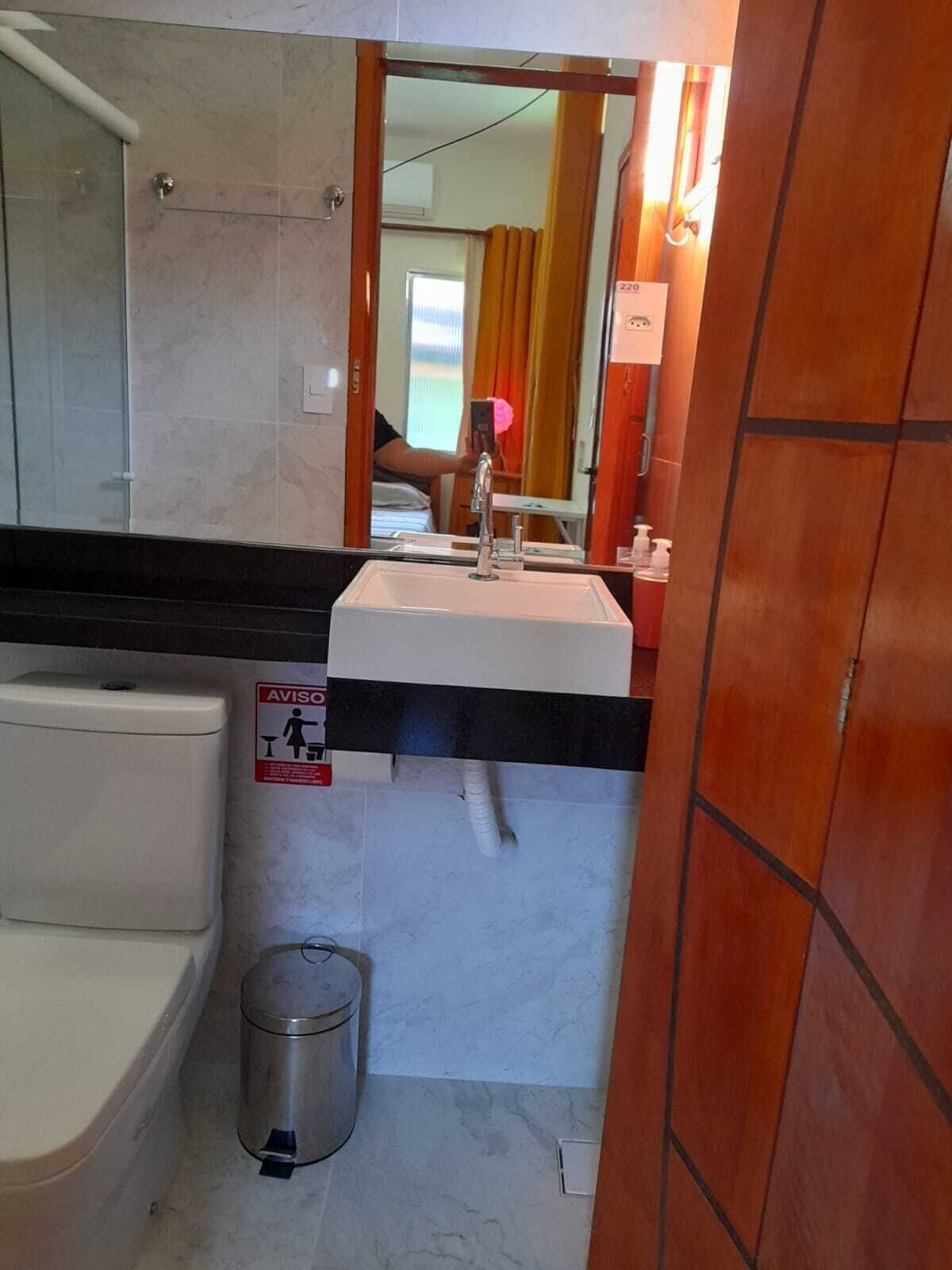 Casa de banho com lavatório, espelho, sanita e caixote do lixo.
