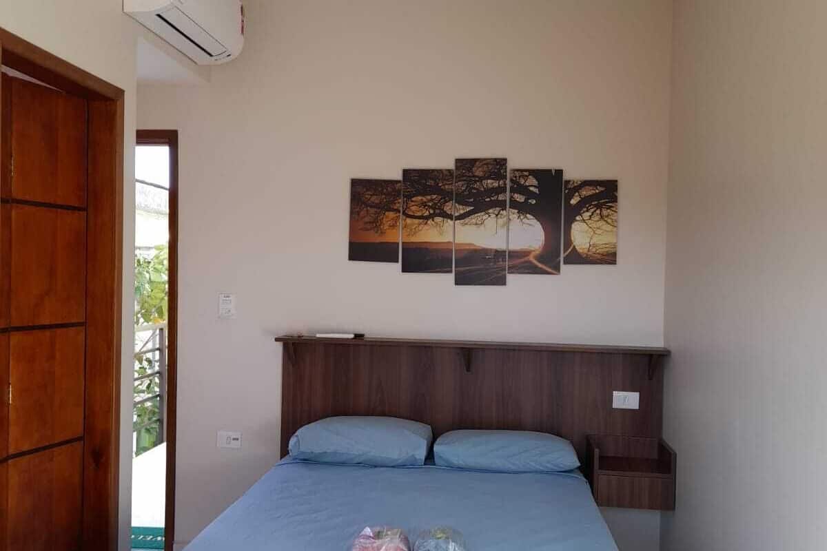 Ein Schlafzimmer mit einem Bett, einem Holzkopfstück, einer Wand-Klimaanlage und einem dreiteiligen Kunstwerk über dem Bett.
