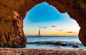 A coastal scene with a sailboat on the water, viewed through a rocky arch. - MAHO BEACH VIEW (MAHO)
