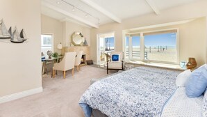 A bedroom with a large bed, a desk, a chair, and a view of the beach.