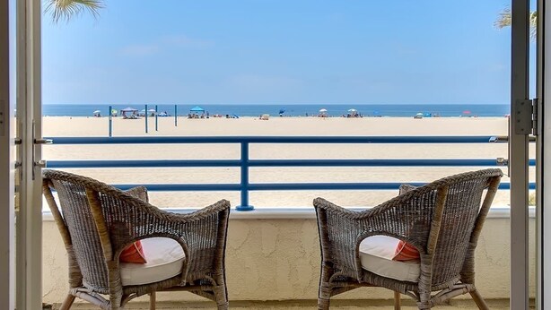 A balcony with wicker chairs facing a beach.
