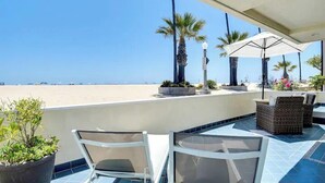 A terrace with a view of the beach, outdoor furniture, and potted plants.