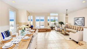 A spacious living area with a long dining table set for a meal, a comfortable sofa, and a view of the sea.