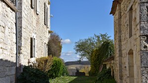 Un stretto vicolo delimitato da edifici in pietra, con una zona verde e alberi al centro.