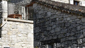 Un edificio in pietra con tetto in tegole, un balcone con ringhiera metallica e una piccola finestra.