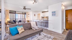 Een moderne woonkamer met een grijze bank, een glazen eethoek en een keuken op de achtergrond.