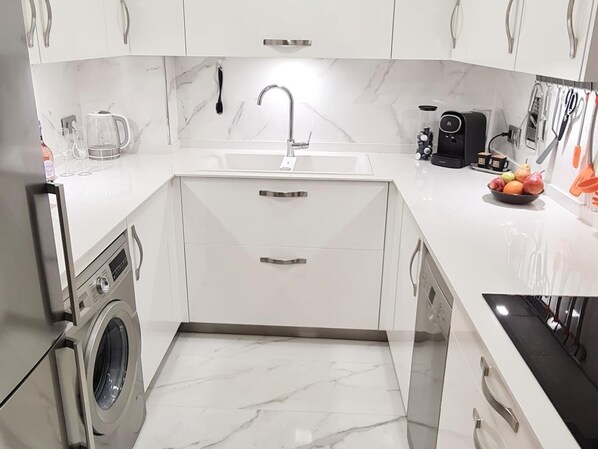 Une cuisine compacte équipée d’un lave-linge intégré, d’un évier et d’une machine à café.