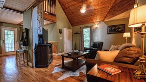 A cozy living room with a wooden ceiling, a fireplace, a sofa, a coffee table, and a lamp. - DOG FRIENDLY! Less than a mile from Dollywood and a min drive to the Parkway (Pigeon Forge)