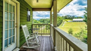 A porch with a rocking chair and a table, overlooking a green landscape with a building in the distance. - DOG FRIENDLY! Less than a mile from Dollywood and a min drive to the Parkway (Pigeon Forge)