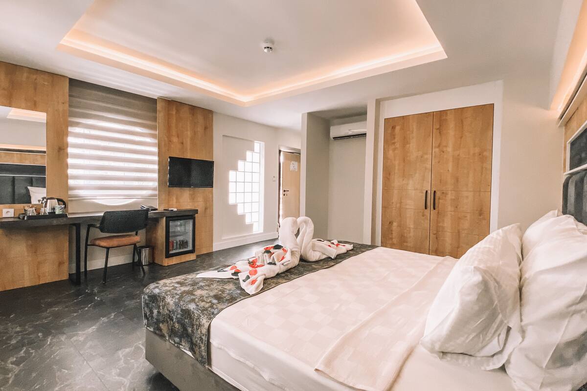 A modern hotel room with a bed, a desk, a chair, a wardrobe, and a bathroom door.
