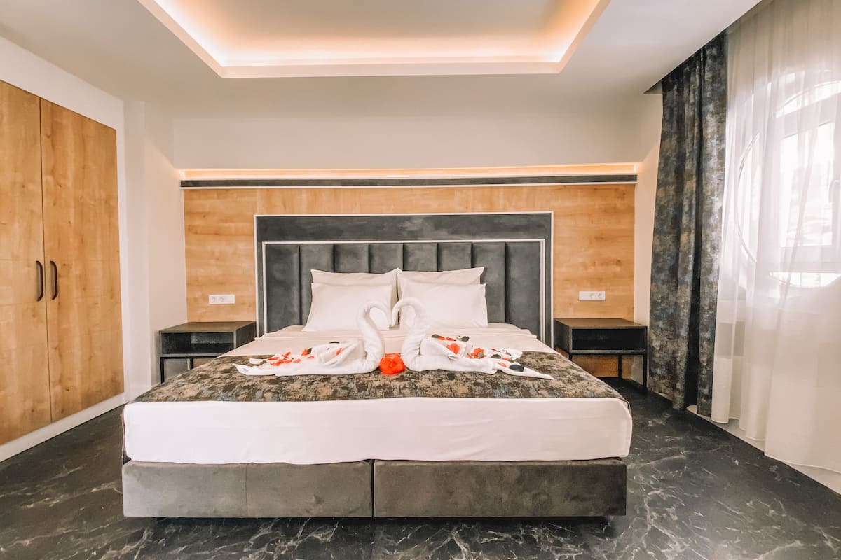 A modern hotel room with a large bed, wooden wardrobe, and a marble floor.