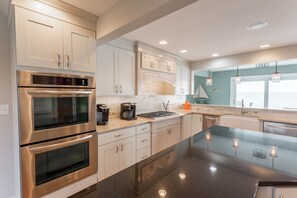 Une cuisine moderne dotée d’appareils électroménagers en acier inoxydable, de meubles blancs et d’un grand îlot central agrémenté de luminaires suspendus.