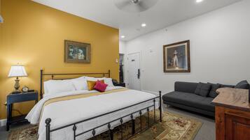 A bedroom with a bed, a nightstand, a lamp, a gray sofa, and two framed pictures on the walls.