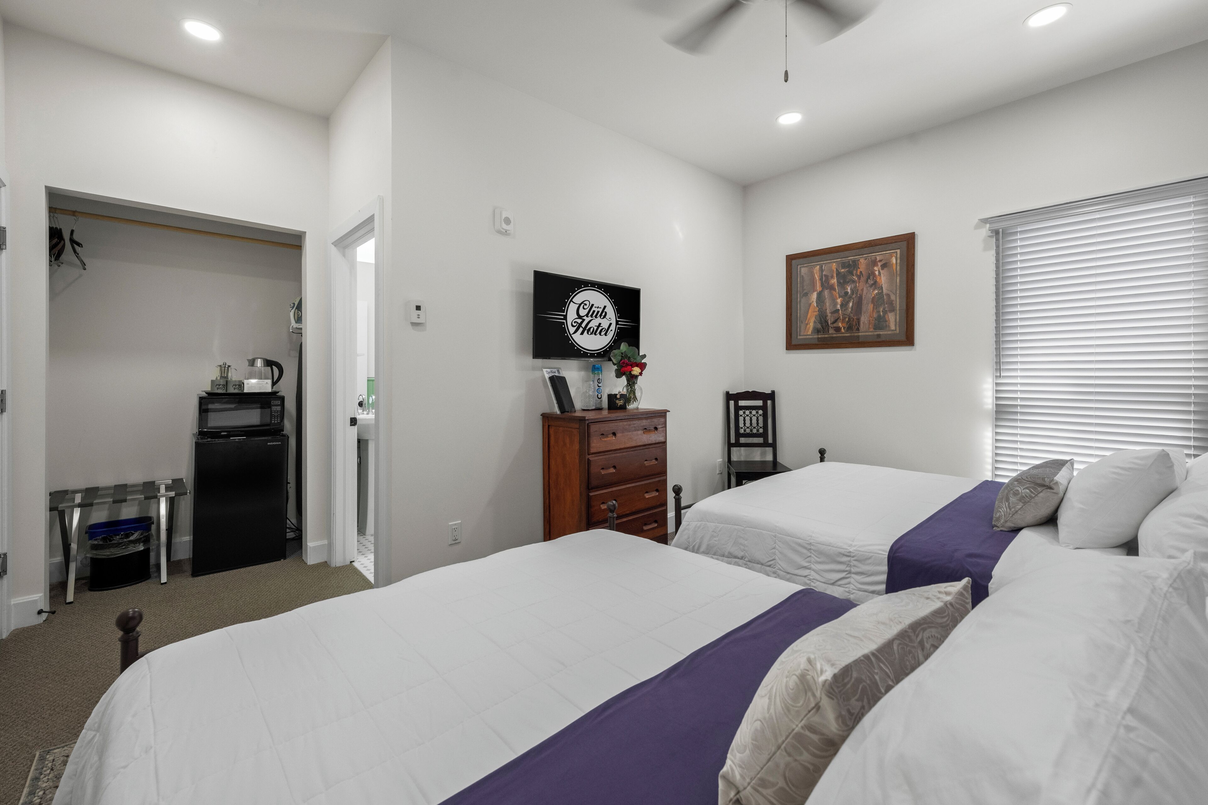 A hotel room with two beds, a desk, a television, and a painting on the wall.