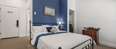 A bedroom with a bed, a nightstand, a dresser, a door, and a blue accent wall.