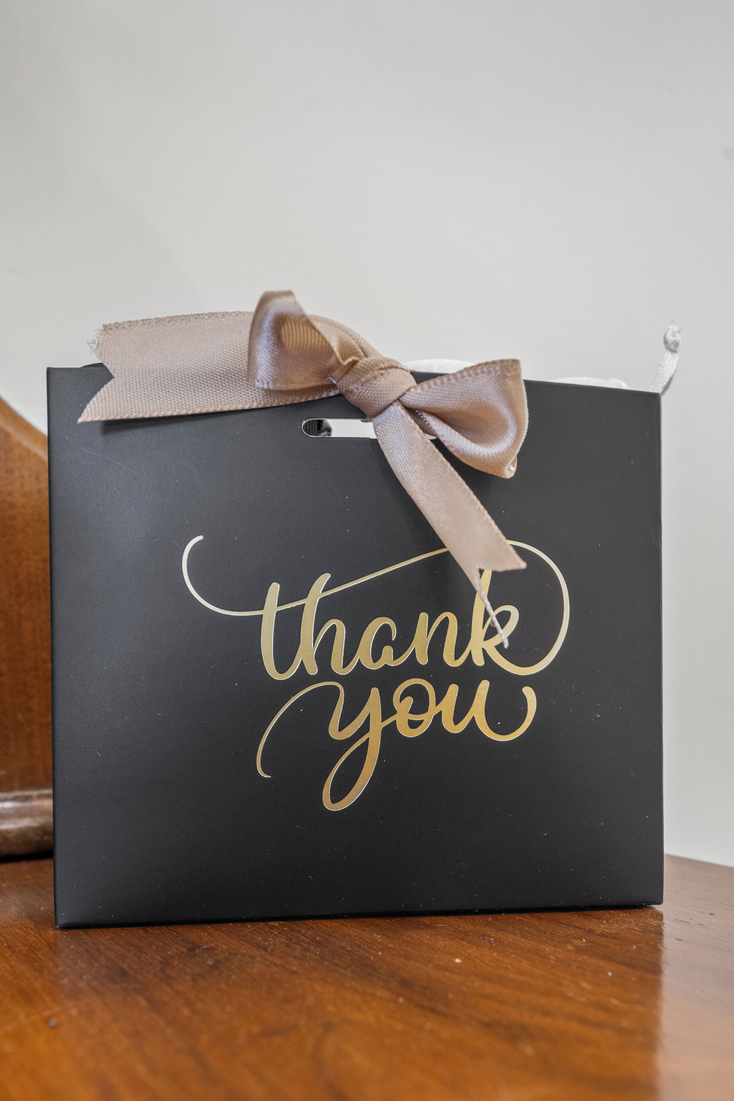 Een zwarte geschenkzak met een gouden lint en de tekst 'thank you' in gouden letters.