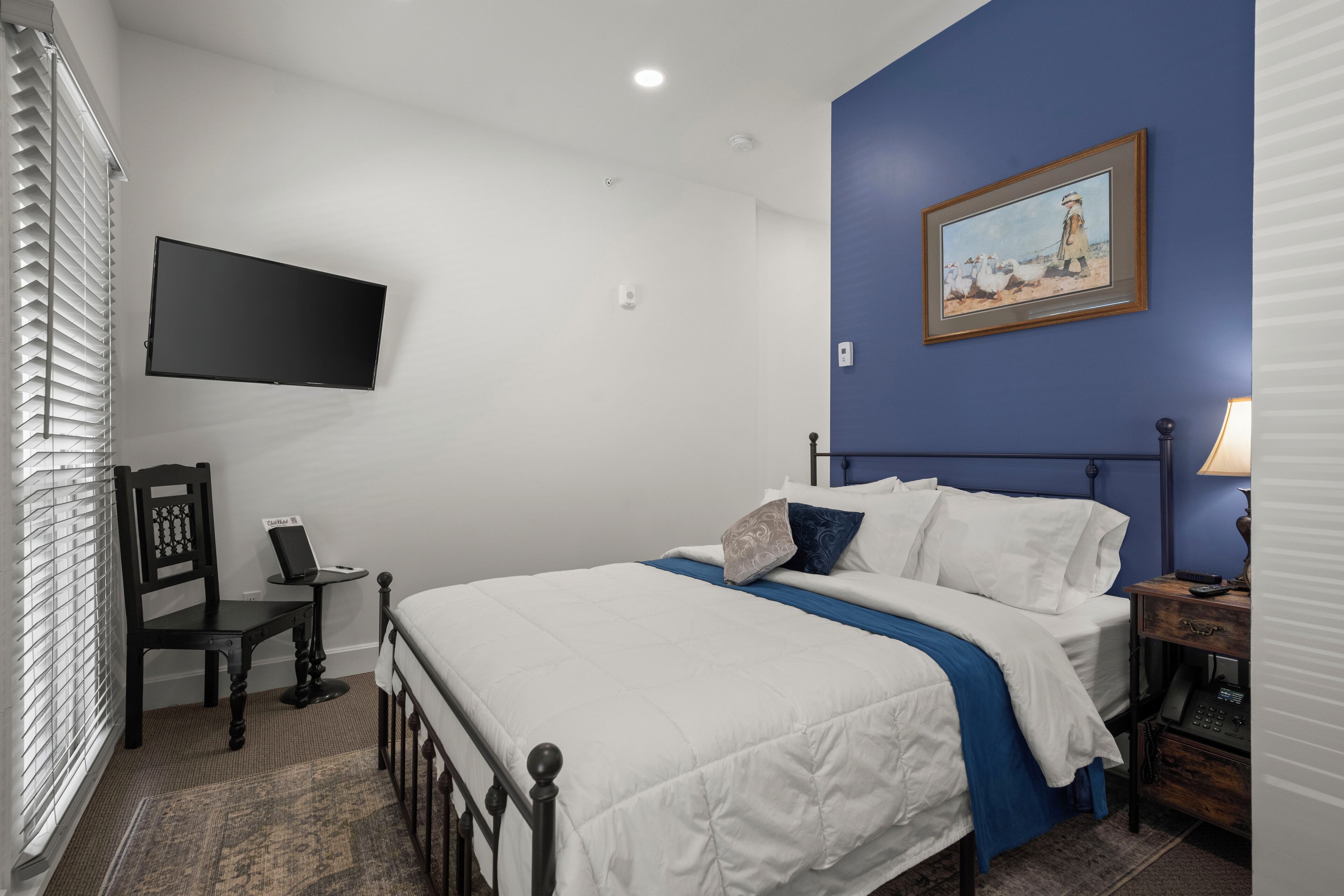 A bedroom with a bed, a desk, a chair, a TV, and a painting on the wall.
