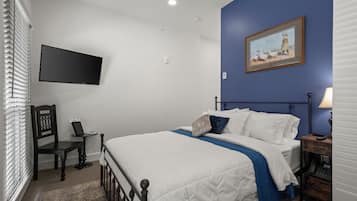 A bedroom with a bed, a desk, a chair, a TV, and a painting on the wall.