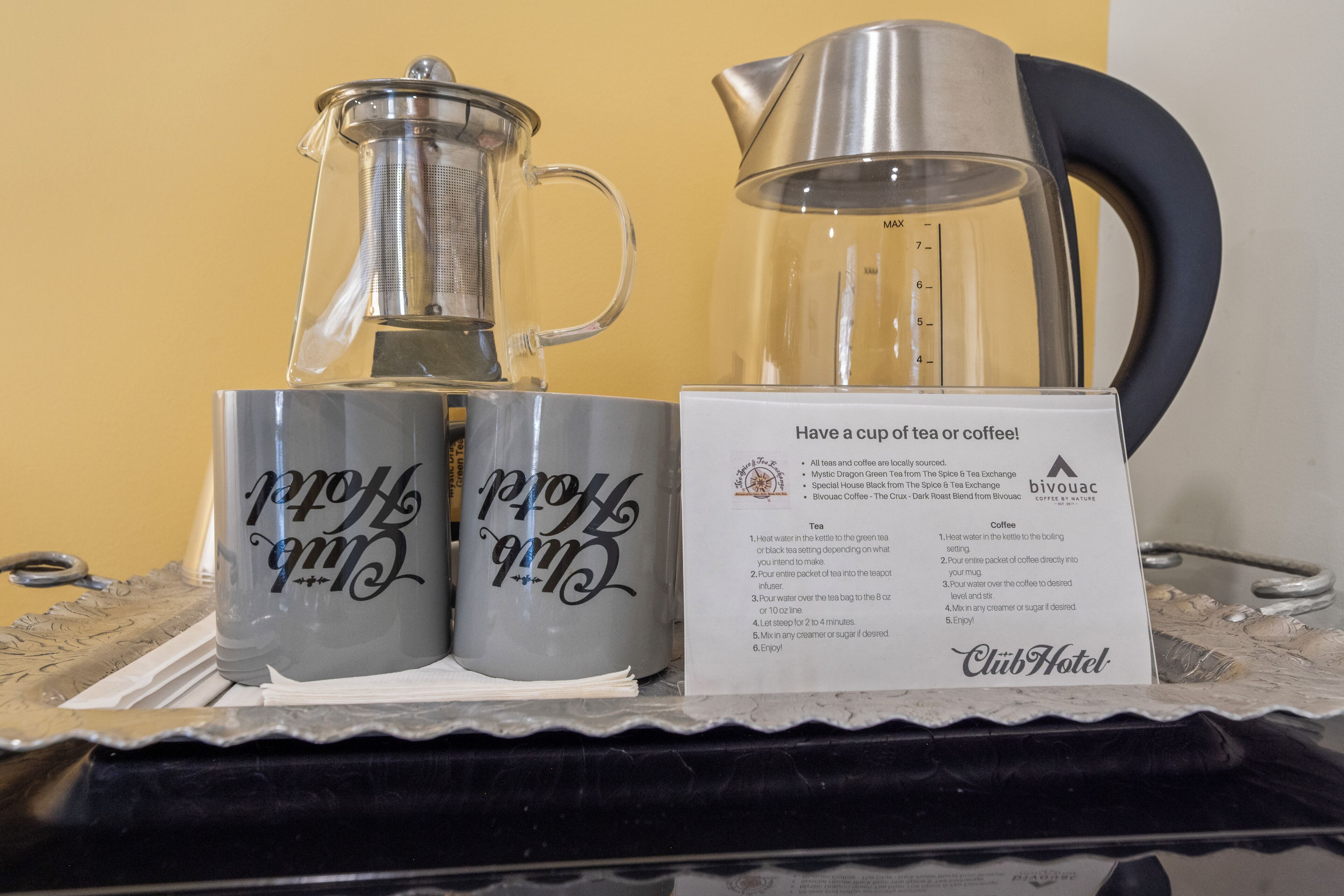 A tea and coffee station with two mugs and a kettle, a sign with instructions, and a tray.